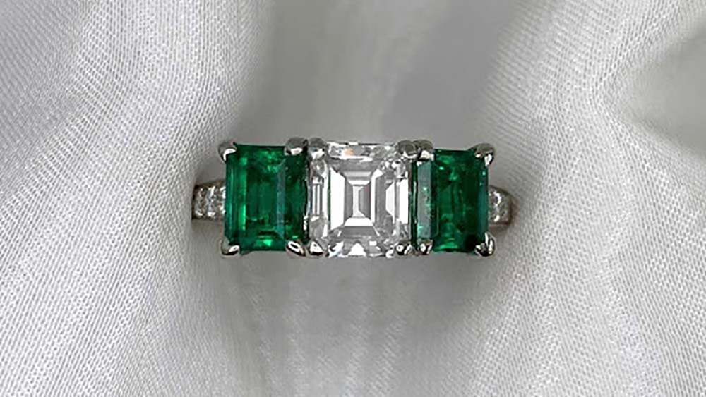 three stone platinum ring with a center diamond and emerald side diamonds