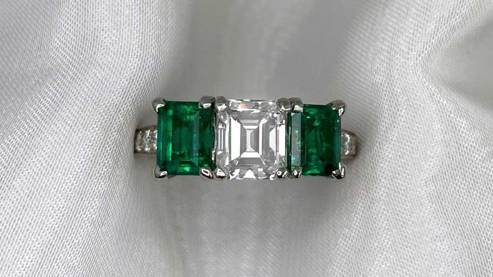 A three-stone ring featuring two emeralds and a diamond.