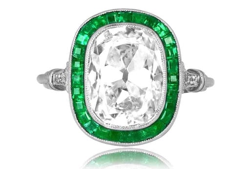 antique cushion cut diamond ring in platinum with a halo of green carre cut emeralds